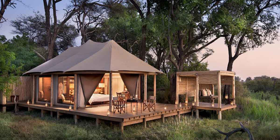 Interior of a luxury tented camp suite in Tanzania's Serengeti with king bed, outdoor shower and private deck overlooking the open plains