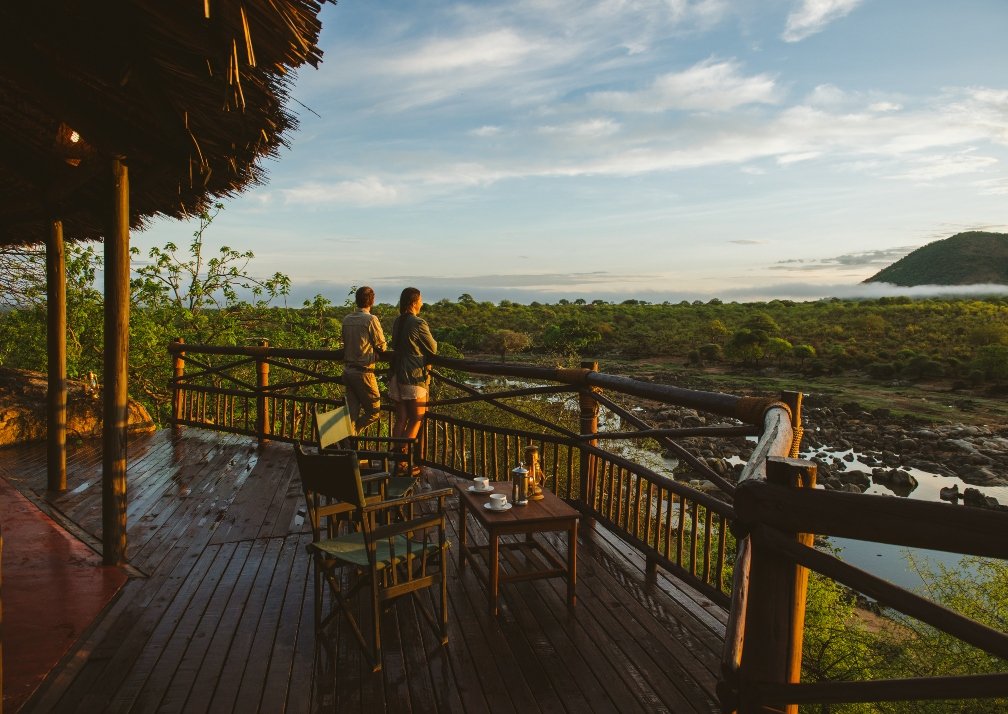 Luxury safari lodge on the banks of the Great Ruaha River in Tanzania at dusk with hippos visible in the water and elephants crossing downstream
